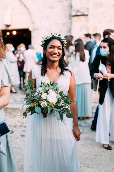 mariée souriante avec couronne de fleurs et bouquet de fleurs blanches et feuillages