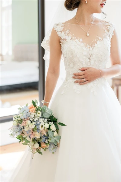 mariée tient son bouquet de mariée bleus et clairs