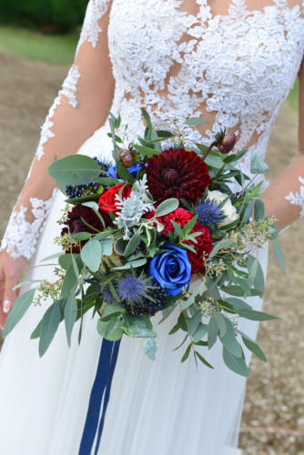 Bouquet de mariée rond déstructuré dans les tons bleus et rouges en roses, dahlias et feuilles d'eucalyptus
