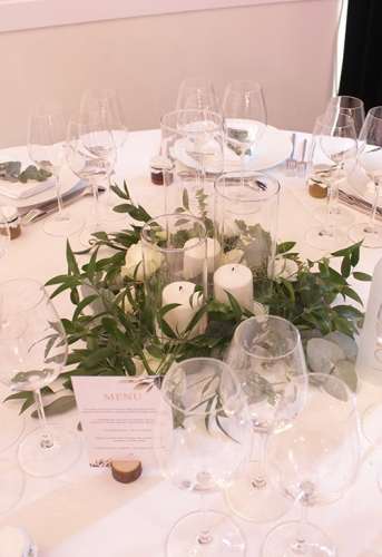 Trio de vases avec bougies entouré d'une couronne de feuillages et quelques fleurs blanches aromatique fleuriste mariage