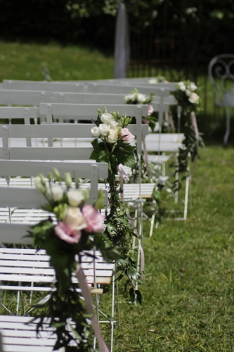 Allée de cérémonie fleurie avec bouquet rose sur les chaises, feuillage retombant aromatique fleuriste mariage